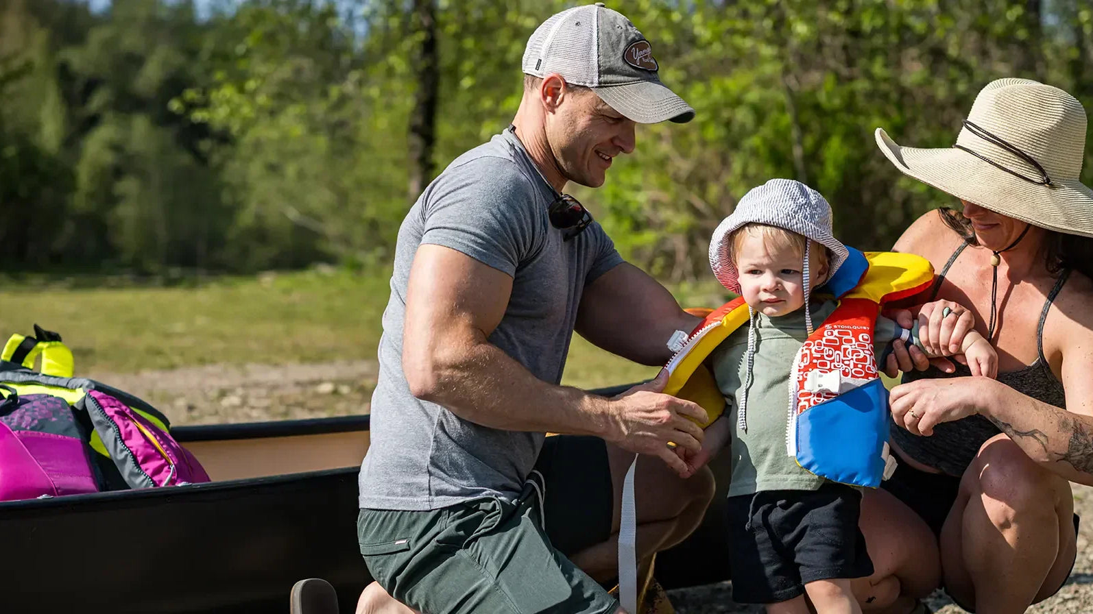 Family outdoors fitting child with Stohlquist life jacket beside kayak and paddling gear