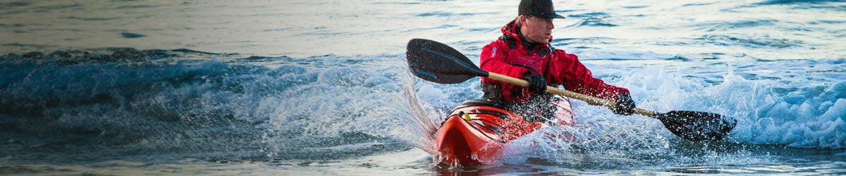 Kayaker in red jacket paddling through waves, showcasing Stohlquist kayaking gear on water.